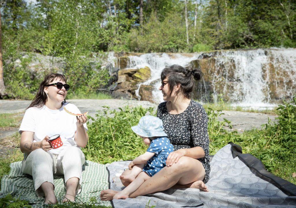 Två personer och ett barn sitter på en filt vid ett vattenfall vid Forsaleden
